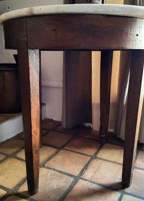 une petite table en bois avec un plateau en marbre, posée sur un sol carrelé