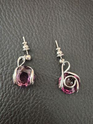 une paire de boucles d'oreilles roses et argentées posées sur une surface en cuir noir