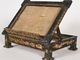 une photo d'un bureau en bois peint en noir et or, sur lequel repose un coussin beige
