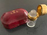 un petit étui rouge avec un couvercle doré, à côté d'un petit flacon en verre