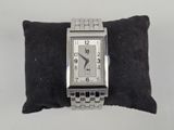 a silver watch on a black pillow on a white surface