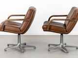 two brown leather office chairs sitting next to each other on a concrete floor