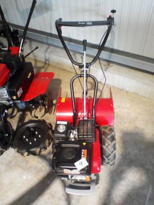 un petit tracteur rouge garé à côté d'une petite tondeuse rouge
