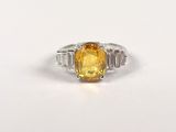 a close up of a yellow sapphire and diamond ring on a white surface