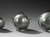 trois théières en argent et deux tasses posées sur une table