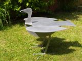 a metal sculpture of a duck on a stand in the grass
