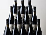 six bottles of wine sit on a wooden table in front of a white wall