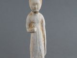 une vieille statue représentant une femme coiffée d'un chapeau, avec une poire posée par terre