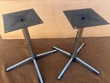 une paire de pieds de table en métal noir posés sur un sol recouvert de moquette marron