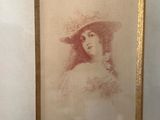 painting of a woman wearing a hat in a gold frame on a wall
