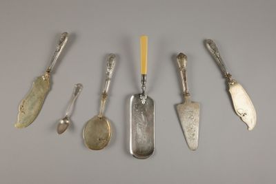 Plusieurs cuillères et couteaux en argent sont alignés sur une table
