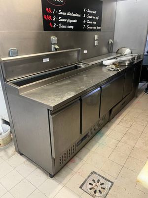 un plan de travail en acier inoxydable dans la cuisine d'un restaurant, avec un panneau affichant le menu accroché au mur