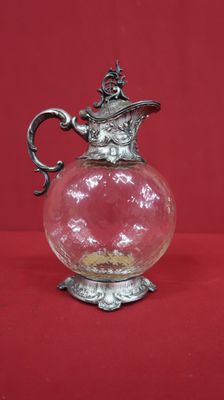 a glass vase with a silver handle on a red background