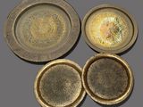 three brass plates and a bowl on a gray surface