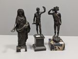 trois statues en bronze représentant une femme et un homme, posées sur des socles en marbre