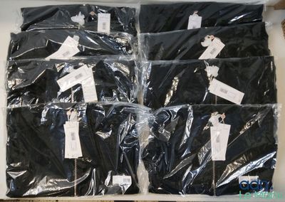 six paires de chemises noires emballées dans du plastique, posées sur une table
