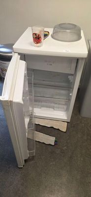 a small white refrigerator with its door open next to a toilet
