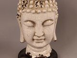 statue représentant une tête de Bouddha posée sur un socle en bois, avec un fond gris