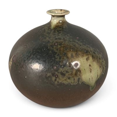 un vase marron et noir posé sur une surface blanche