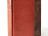 an old book sitting on top of a white table next to a red book