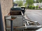 des voitures garées sur un parking à côté d'un immeuble où s'entasse un tas de vieilleries