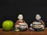 two figurines sitting next to an apple on a table
