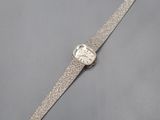 une montre argentée posée sur une surface grise, sur fond blanc