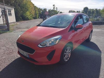 La voiture rouge est garée sur le parking, à côté d'une clôture.