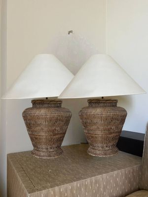 pair of wicker lamps with white shades on top of a table