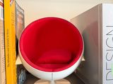 a red ball chair sitting on a book shelf next to a book