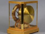 a gold clock in a glass case on a gray surface