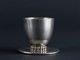 an antique silver cup on a saucer on a black background