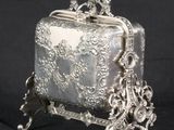 an antique silver purse on a stand against a black background