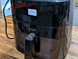 une friteuse à air chaud noire posée sur une table en bois dans un entrepôt
