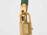 a close up of a watch with a green strap and gold clasp