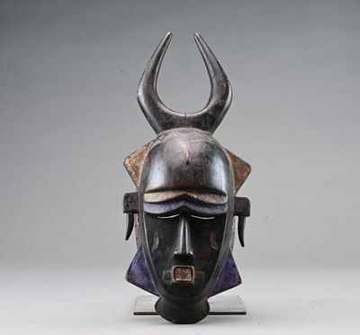 un masque africain muni de cornes, posé sur un socle, sur fond gris