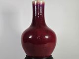 un vase rouge posé sur un socle noir, lui-même posé sur une surface blanche