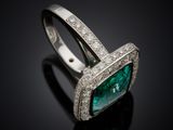 an emerald and diamond ring on a black surface