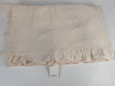 une photo d'un oreiller blanc aux bords festonnés posé sur une surface blanche