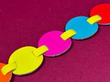 a close up of a colorful paper chain on a pink surface