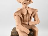 statue d'un homme coiffé d'un chapeau, assis sur un bloc de bois