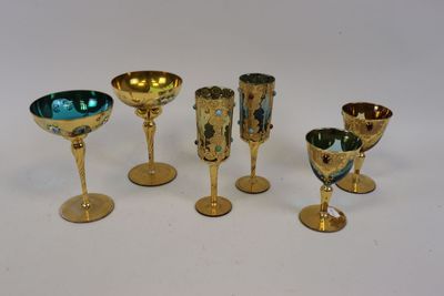 six gobelets et coupes en or sont alignés sur une surface blanche