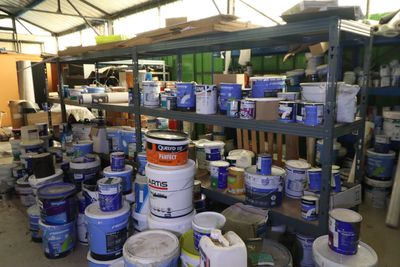 de nombreux seaux de peinture posés sur une étagère dans un entrepôt