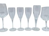 six clear wine glasses lined up in a row on a white surface