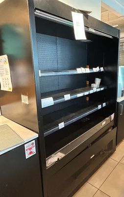 un réfrigérateur vide dans un magasin où de nombreuses étagères sont vides