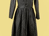 un manteau noir posé sur un pied de mannequin, devant un fond jaune