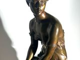 bronze statue of a boy sitting on a rock with his hands on his knees