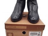 des bottines en cuir noir posées sur une boîte en carton, sur fond blanc