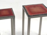 two metal tables with red glass tops sit on a white surface