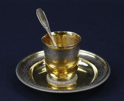 une tasse en argent contenant une cuillère, posée sur une assiette en argent